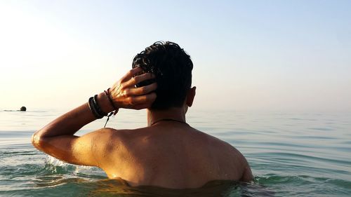 Man photographing with camera on sea against clear sky