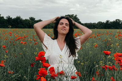 Beautiful young woman on red poppy at field against sky