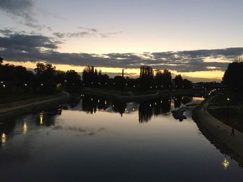 Silhouette trees by river against sky during sunset