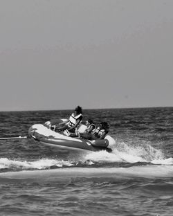 Friends enjoying on inflatable raft amidst sea against sky