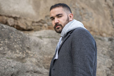 Caucasian man standing on a rock outdoors wearing grey winter coat