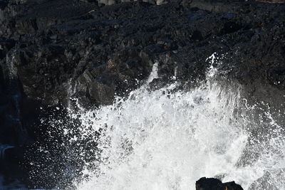 High angle view of sea waves splashing on rock