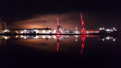 Illuminated factory by river against sky at night