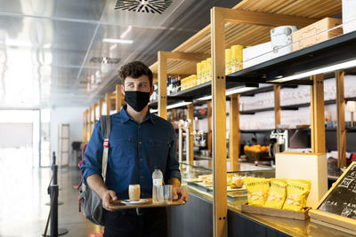 Businessman in protective face mask holding tray of drinks in cafe during covid-19