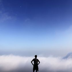 Rear view silhouette man standing against clouds with hands on hips