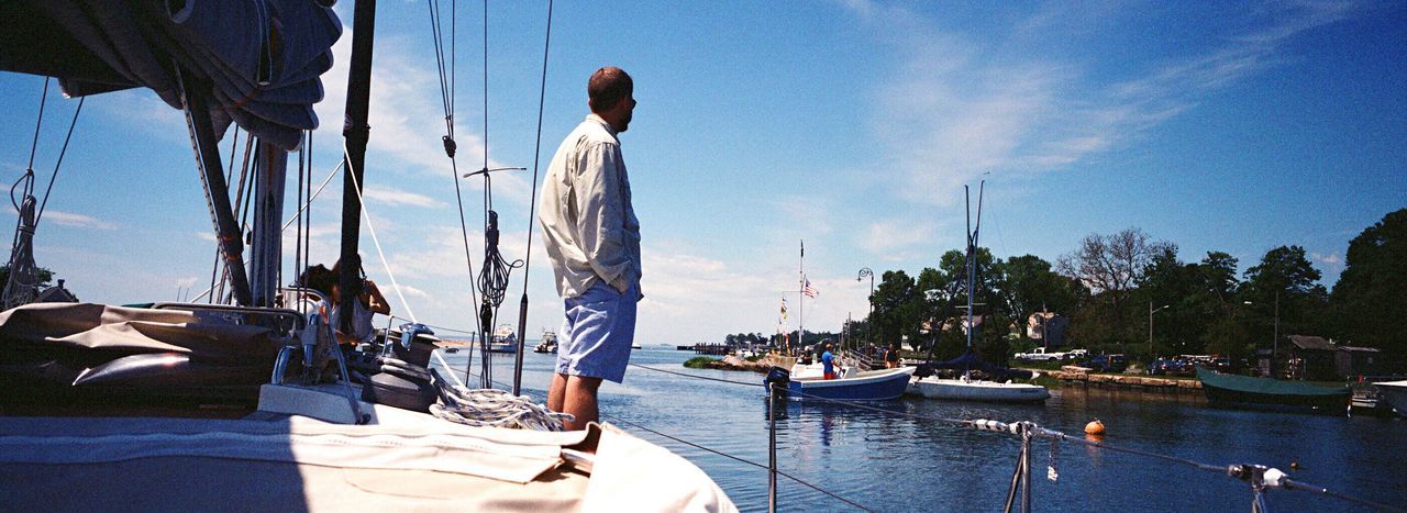 nautical vessel, mode of transport, transportation, boat, real people, sky, water, one person, men, day, moored, sea, outdoors, harbor, mast, yacht, sailing, sailboat, standing, nature, tree, architecture, one man only, people