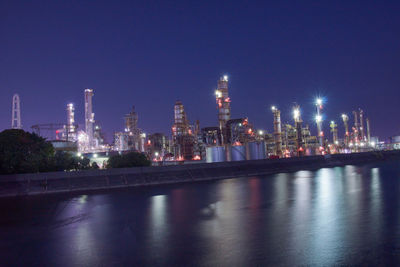 Illuminated buildings by river against sky at night