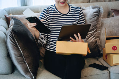 Midsection of woman using digital tablet while sitting on sofa at home