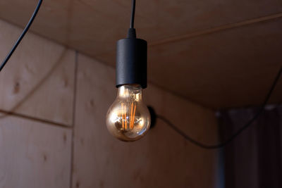 Low angle view of illuminated light bulb hanging on ceiling