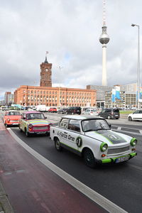 Cars on road by buildings against cloudy sky