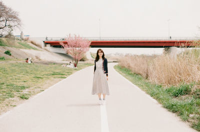 Full length of woman standing on street by bridge against clear sky