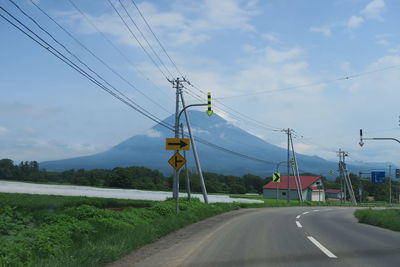 Electricity pylons by road against sky