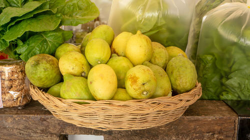 Yellow and green skin lemons in a brown basket, fresh organic lettuce vegetable in plastic bag 