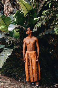 Full length of shirtless man standing against tree