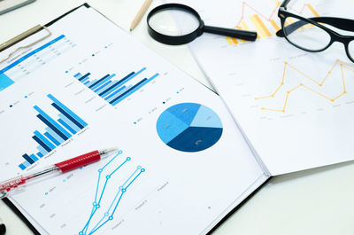 High angle view of chart papers with pen and eyeglasses on desk