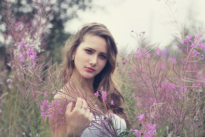 Portrait of beautiful young woman by purple flowering plants against sky
