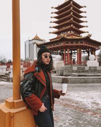 Portrait of young woman standing against building in city