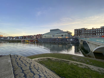 Bridge over river by buildings in city against sky