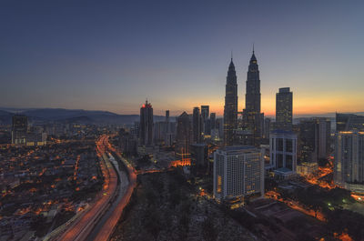 Petronas towers amidst buildings against sky during sunrise