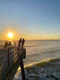 People on beach against clear sky during sunset