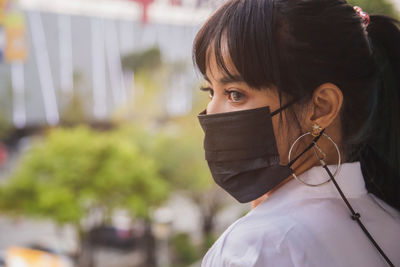 An asian woman in a white shirt wearing a face mask standing in front of a urban building