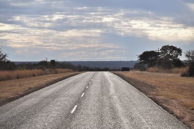 Empty road amidst field against sky