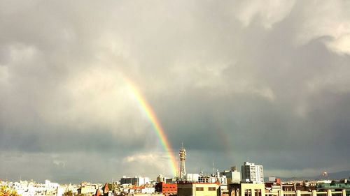 Rainbow over city against cloudy sky