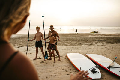 Female instructor giving course of paddleboarding to tourists at beach during sunset