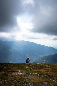 Woman sitting on mountain against sky