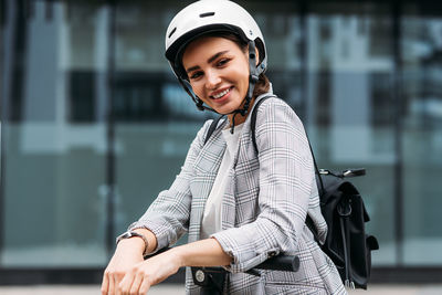 Portrait of cheerful businesswoman in white cycling helmet looking at camera leaning on handlebar 