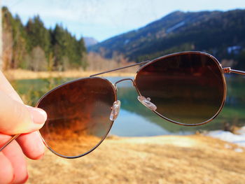 Close-up of hand holding sunglasses against sky