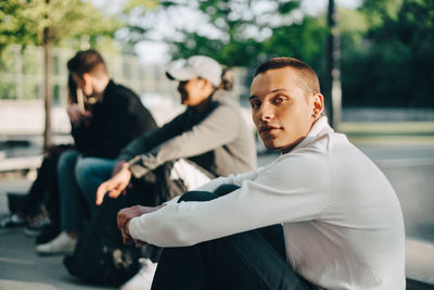 Portrait of young man sitting with friends at park