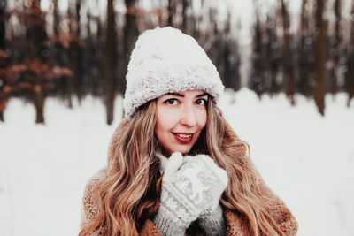 Beautiful young woman in snowy fancy winter woodland. girl wearing fluffy gloves, cap and coat