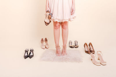 Stylish girl standing in pink pleated dress surrounded by a variety of shoes. 