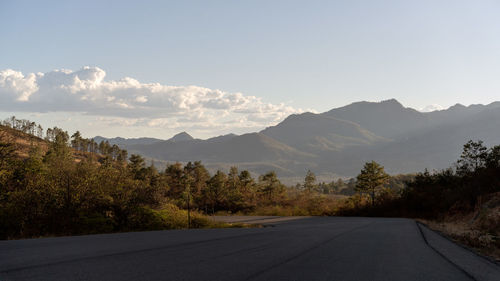 Empty road along trees and mountains against sky