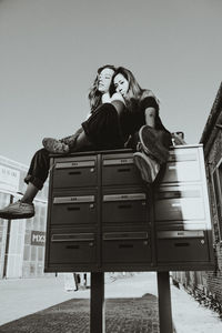 Black and white portrait of 2 women chilling on a postbox 