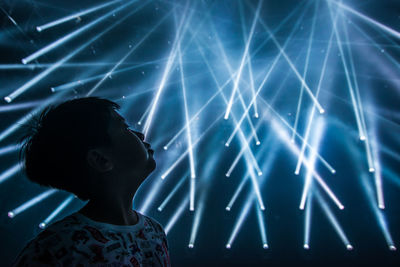 Boy looking away while standing against illuminated lights