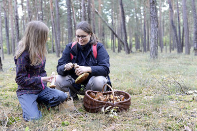 Woman with daughter collecting edible mushroom in basket at forest
