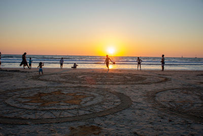 People on beach against clear sky during sunset