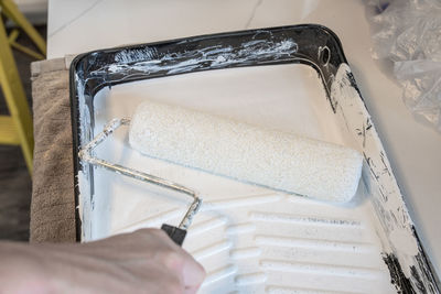 Hand holds a paint roller in a paint tray with white paint for your project