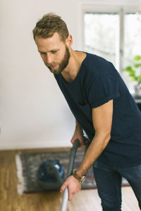 Young man vacuuming floor at home