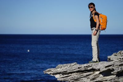 Man standing on rock by sea against clear sky