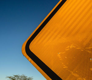Partial view of a yellow traffic sign near a highway