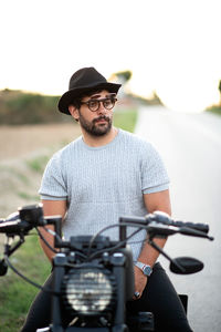 Biker in hat and sunglasses sitting motorcycle at sunset.