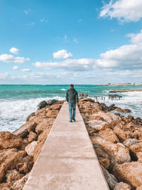 Rear view of woman standing on rock at beach against sky