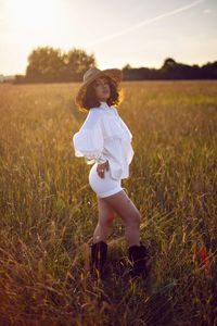 Portrait woman in white clothes and in a wicker hat stand on a field with grass in autumn