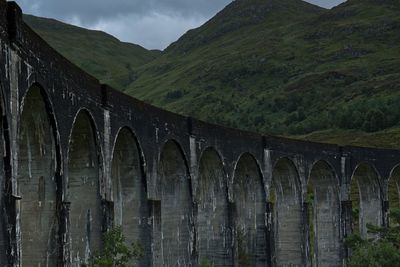 View of stone arch railway bridge amidst trees and mountains 