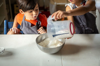 Two girls wearing grey aprons adding sugar to flour