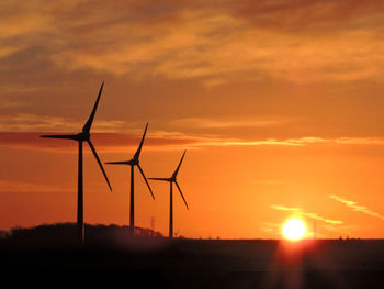 Silhouette windmills against sky during sunset