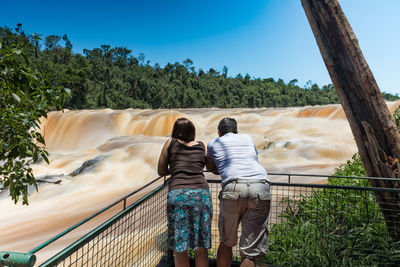 Rear view of couple standing by railing against waterfall